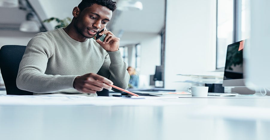  Business professional on a phone call reviewing documents, representing Microsoft Teams Phone licensing and total cost evaluation.Business professional on a phone call reviewing documents, representing Microsoft Teams Phone licensing and total cost evaluation.