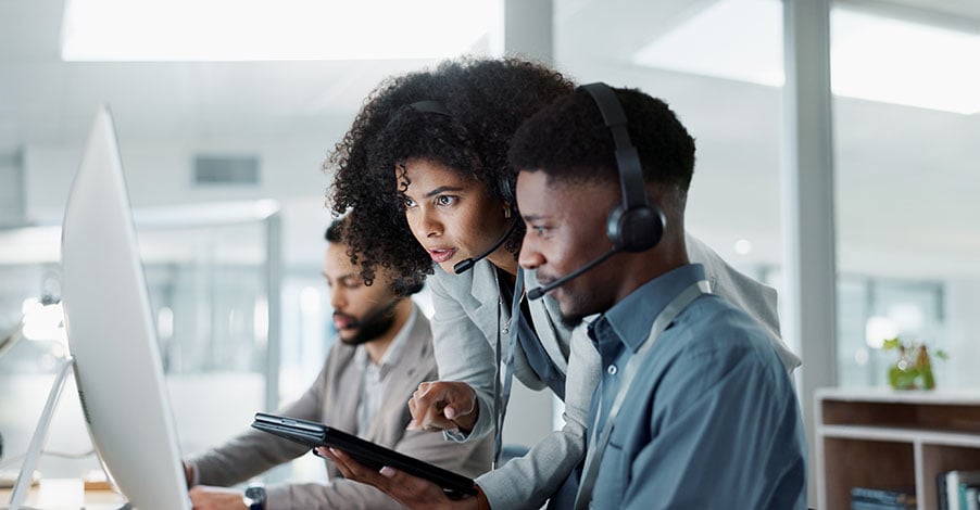 Contact center supervisor coaching an agent at a workstation, representing voice fraud verification and escalation protocols.