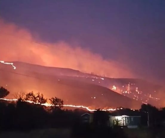 Wildfire burning across a ridgeline above homes in Okanogan County